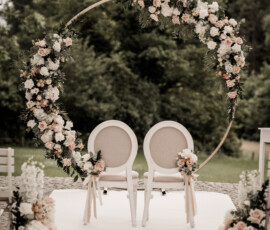 Runder Traubogen mit weißen und roséfarbenen Rosen, floraler Dekoration und Stühlen für eine freie Trauung, gestaltet von der Gärtnerei Reinwald aus Heilbronn. Traubogen mit weißen und roséfarbenen Rosen, Grün und zwei Stühlen für eine freie Trauung im Freien.