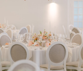 Ein Blütentraum für die Hochzeitsfeier: festlich gedeckte Tische und üppige florale Dekoration in Apricot, Rosa und Weiß schaffen eine romantische Atmosphäre. Festlich gedeckte Hochzeitstische mit apricotfarbener Blumendekoration und üppigem Blumenschmuck an der Decke.