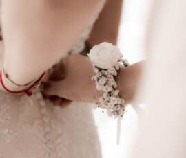 Zarter Blumenschmuck fürs Handgelenk: weiße Blüte und Schleierkraut ergänzen das Hochzeitsoutfit auf elegante Weise. Floraler Handgelenkschmuck mit weißer Blüte und Schleierkraut am Arm der Braut.