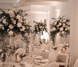 Stilvolle Hochzeitsfloristik von Gärtnerei Reinwald: hohe weiße Blumengestecke, grüne Akzente und festlich gedeckte Tische schaffen eine elegante Atmosphäre. Hochzeitslocation mit runden Tischen und hohen weißen Blumengestecken von Gärtnerei Reinwald Heilbronn.