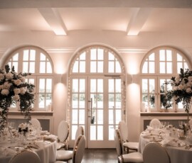 Elegante Hochzeitsfloristik von Gärtnerei Reinwald: hohe weiße Blumengestecke, Kerzen und festlich gedeckte runde Tische schaffen eine stilvolle Atmosphäre. Elegante Hochzeitslocation mit runden Tischen und hohen weißen Blumengestecken von Gärtnerei Reinwald Heilbronn.
