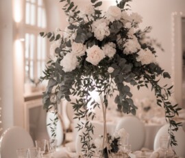 Elegante Hochzeitsfloristik von Gärtnerei Reinwald: ein hohes Blumengesteck mit weißen Blüten und Eukalyptus als stilvoller Mittelpunkt der Hochzeitstafel. Hohe Hochzeitstischdekoration mit weißen Rosen, Blüten und Eukalyptus von Gärtnerei Reinwald Heilbronn.
