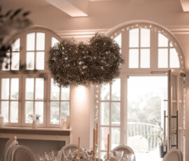 Ein besonderer Blickfang über der Hochzeitstafel: schwebender Blumenschmuck aus Schleierkraut, kombiniert mit weißen Blüten und warmem Kerzenlicht. Festlich gedeckter Hochzeitstisch mit weißen Blumen, Kerzen und schwebender Schleierkraut-Dekoration.