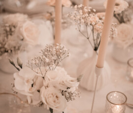 Zarte Blüten, weiße Rosen und warmes Kerzenlicht: eine romantische Tischdekoration für eine stilvolle Hochzeitsfeier Romantische Hochzeitstischdekoration mit weißen Rosen, Schleierkraut und brennenden Stabkerzen.