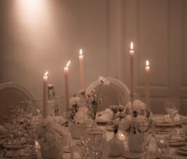 Romantische Hochzeitsstimmung bei Kerzenschein: weiße Blüten, feines Schleierkraut und elegante Tischdetails schaffen eine festliche Atmosphäre. Stimmungsvoll gedeckte Hochzeitstafel mit weißen Blumen, hohen Kerzen und floraler Deckendekoration.